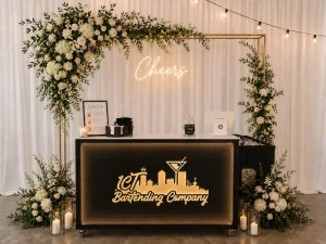 Black portable event bar with illuminated front lettering beneath a floral arch